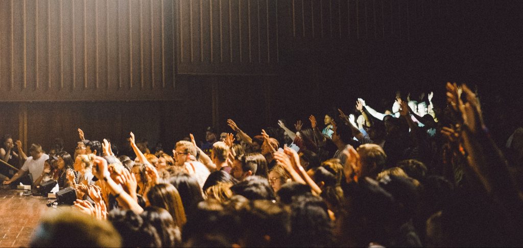 Photo of a crowd in a conference hall, raising their hands. Used to illustrate Reset Connect 2022.