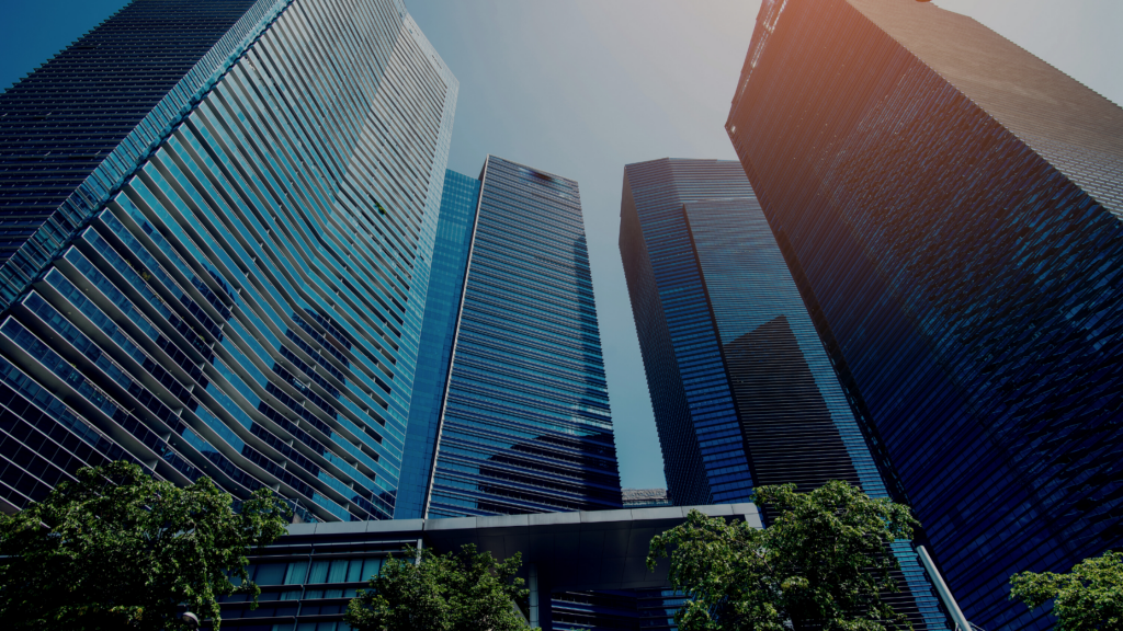 An image of tall buildings with trees visible in the foreground. Image used to illustrate How To Be More Sustainable In The Workplace blog post.