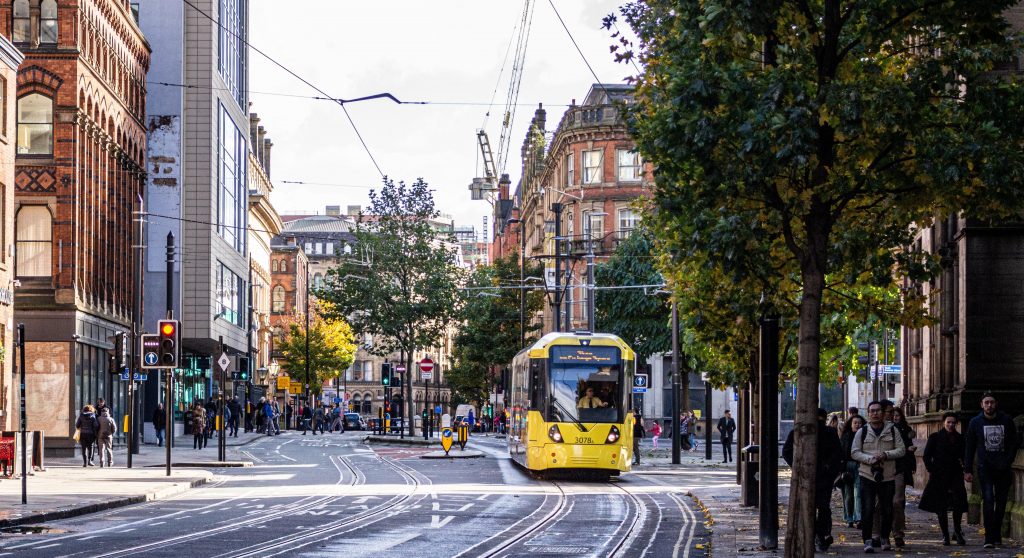 Image of a street in the city of Manchester, with a tram visible as well as some pedestrians. Used to illustrate the blog post entitled Why We Support The Greater Manchester Good Employment Charter.
